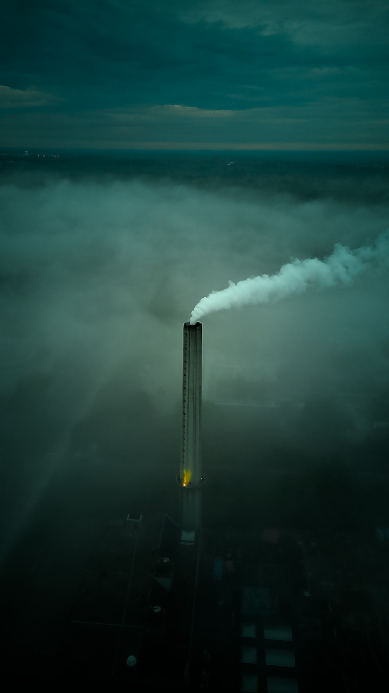 Industrial stack emerging through fog in a cinematic aerial frame.